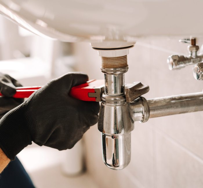 Plumber in black gloves fixes a sink pipe with a wrench in a bathroom, showcasing precision and craftsmanship